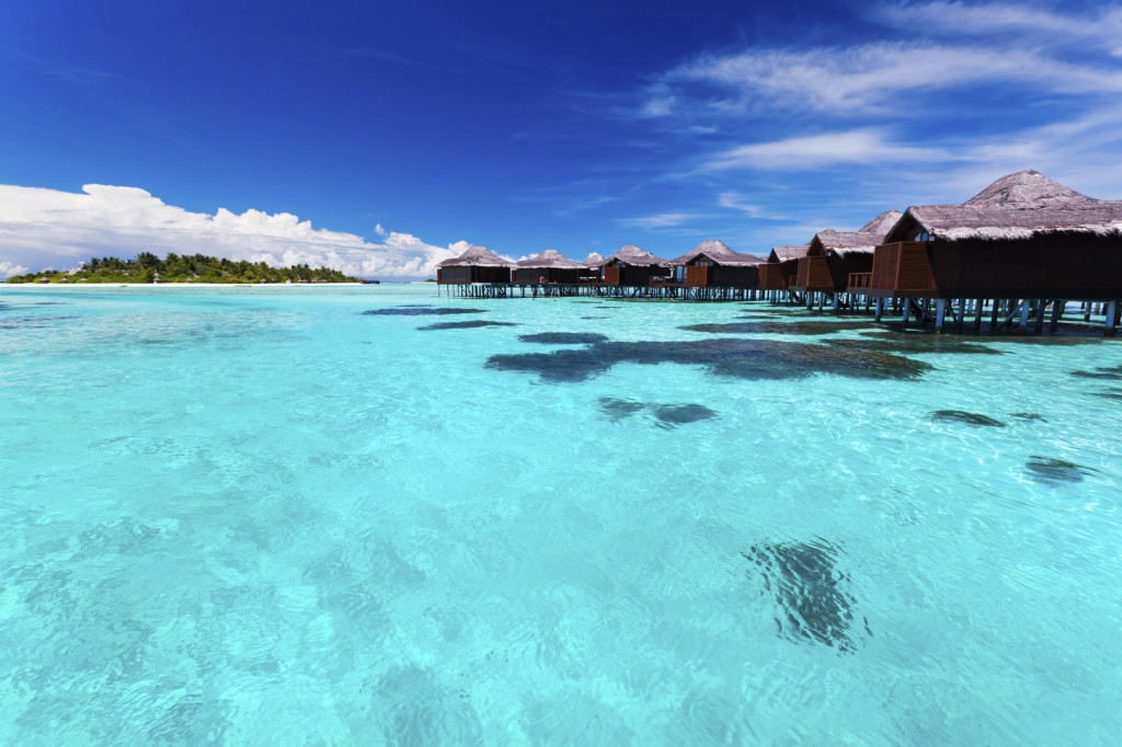 Overwater bungallows in blue lagoon around tropical island