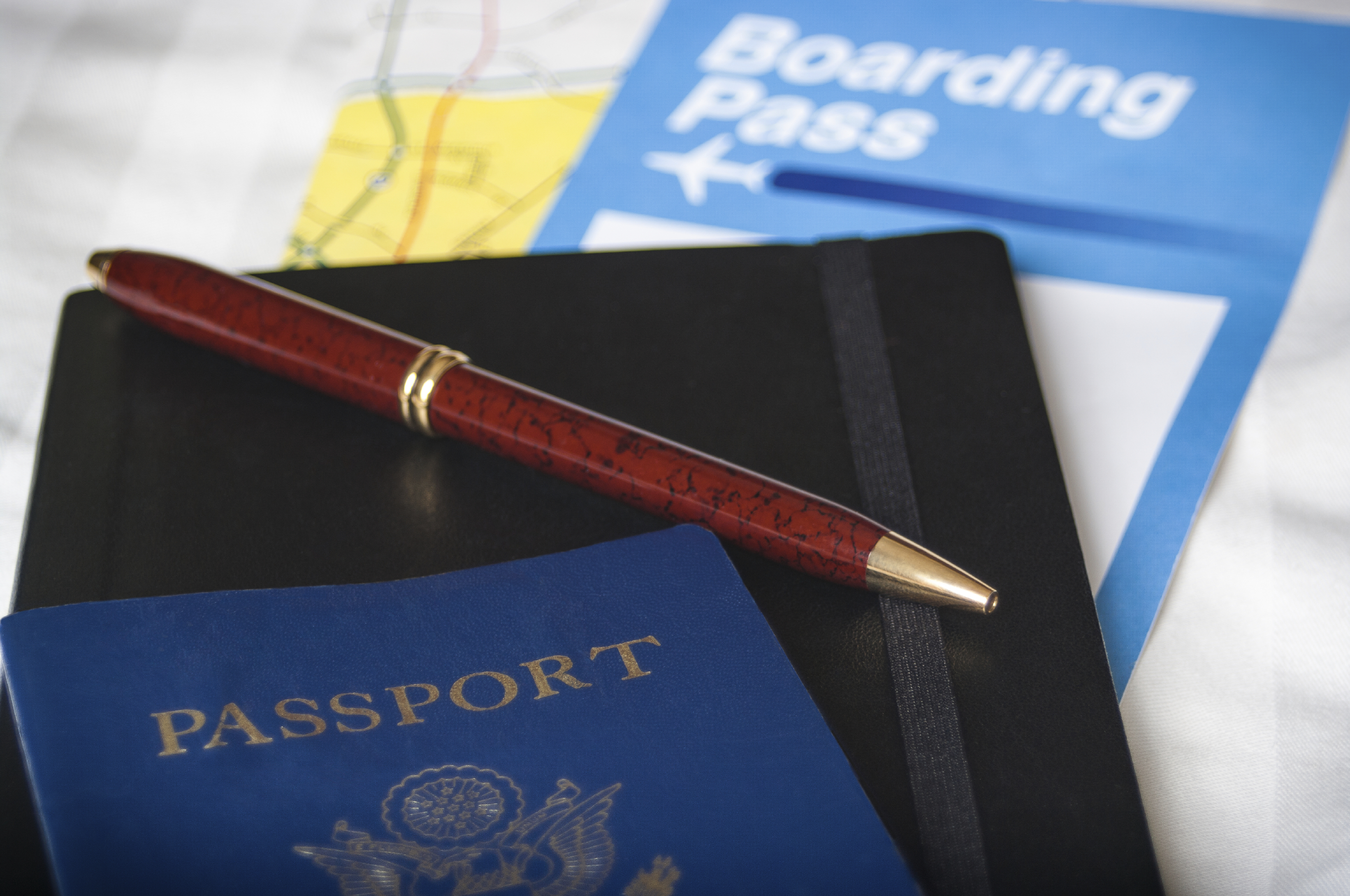 Close-up of a pen on a notebook with a passport. Boarding pass and map in the background. Shot with a shallow depth of field.